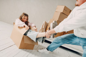 Happy young family couple man carry woman inside box. Moving with cardboard boxes to new estate home apartment concept