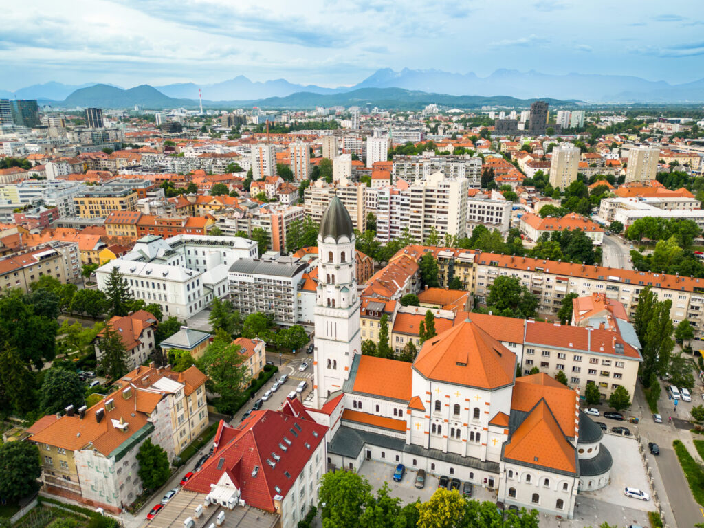 Aerial drone view of Ljubljana, Slovenia. Historical city centre with a church, lush greenery and multiple residential buildings, hills on the background