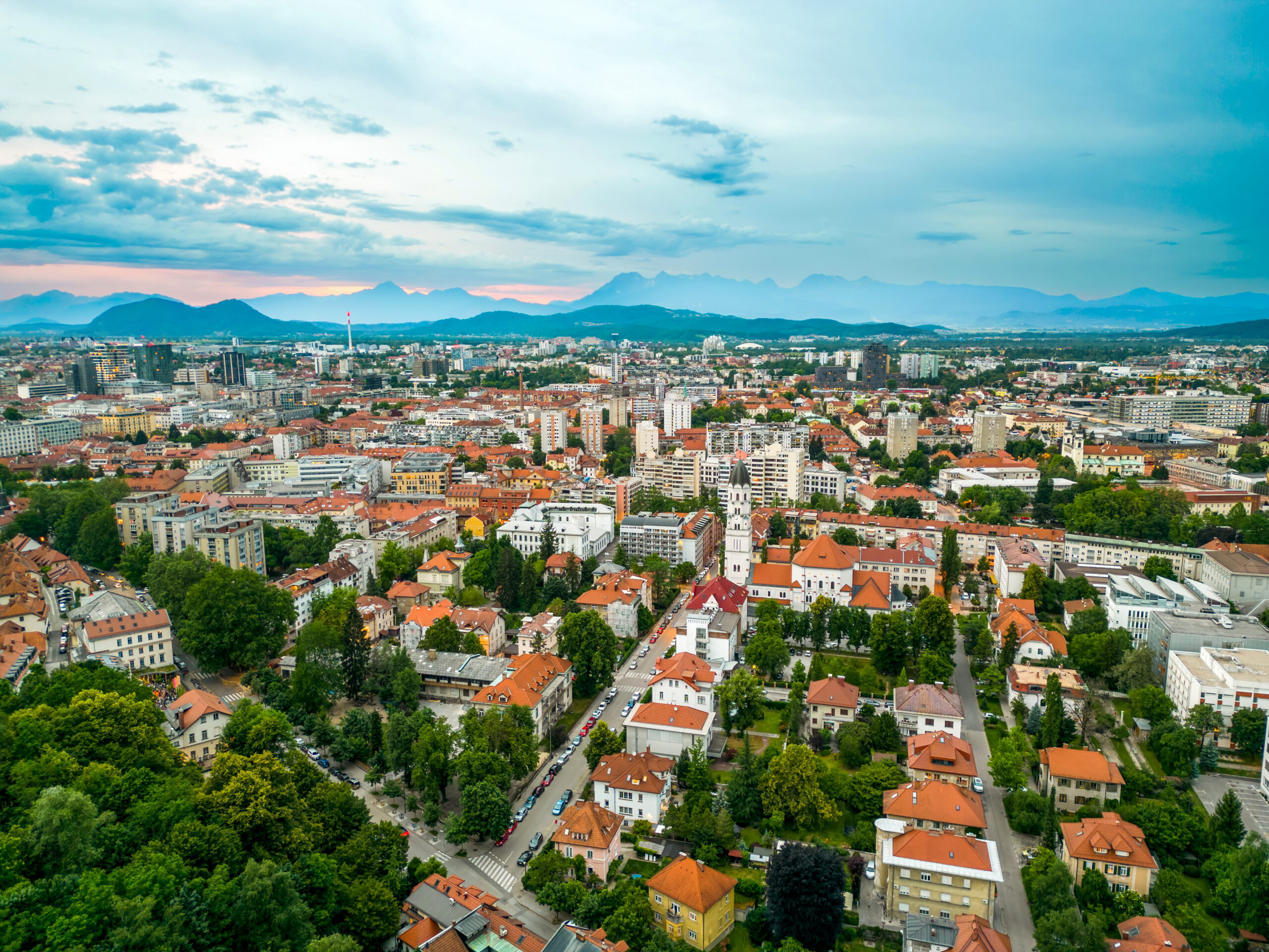 Aerial drone view of Ljubljana, Slovenia. Historical city centre with lush greenery and multiple residential buildings, hills on the background