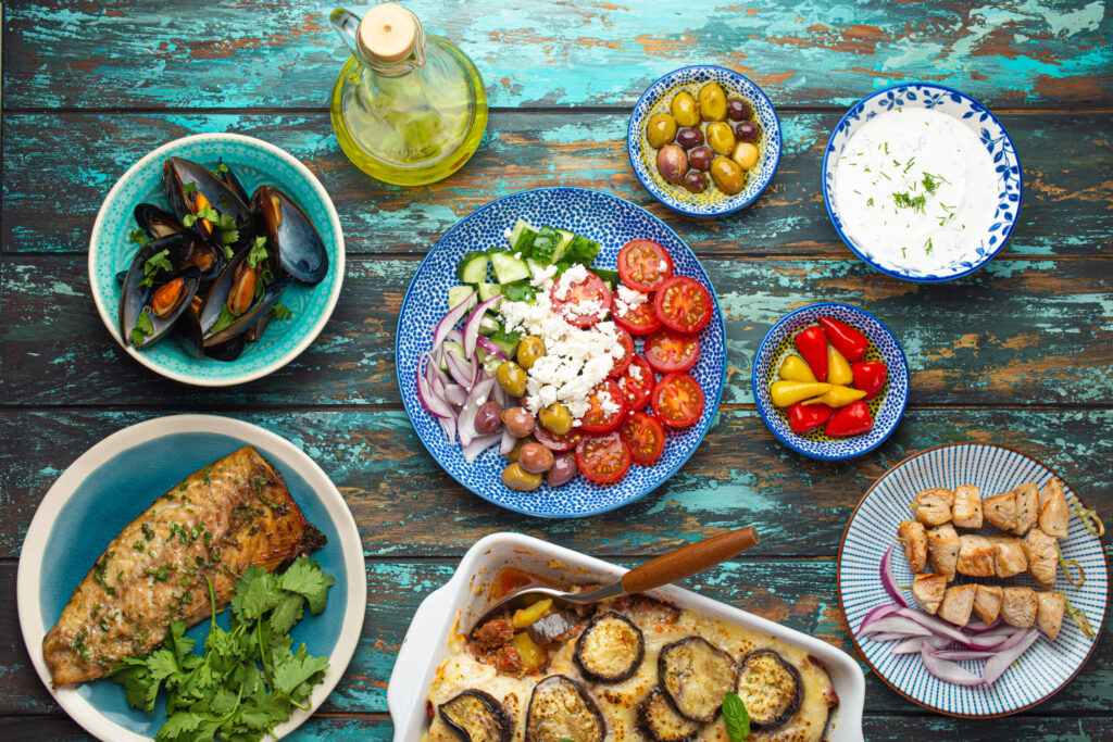 Assorted Greek dishes on rustic wooden background from above, moussaka, grilled fish, souvlaki, greek salad, steamed mussels with herbs, appetizers of Greece from above