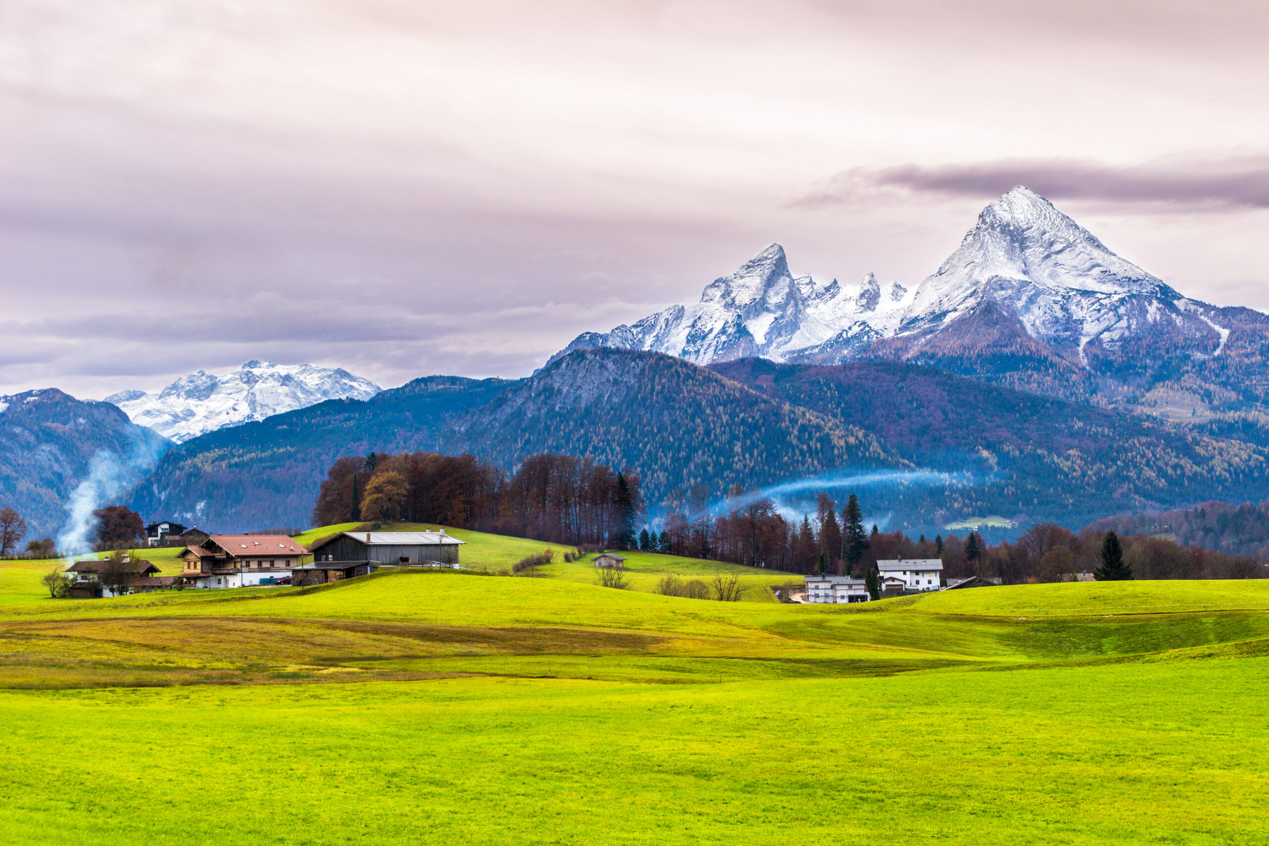 Green meadow, farmer houses and snow-capped Watzmann mountain on a background. Beauty world concept. Bavarian alps. Germany