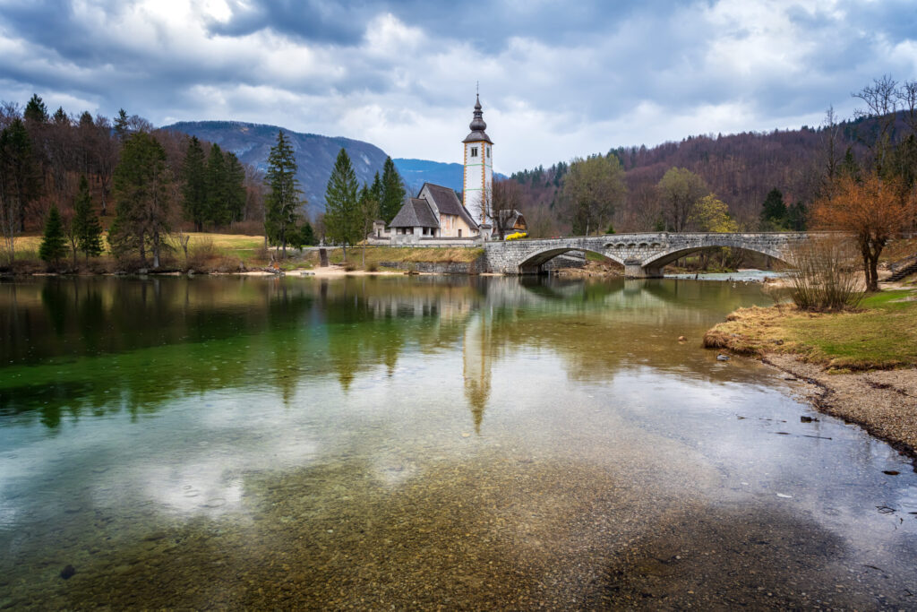 Panoramic spring view of Bohinj lake with the church of St John the Baptist and the stone bridge in Triglav National Park, located in Julian Alps, Slovenia.