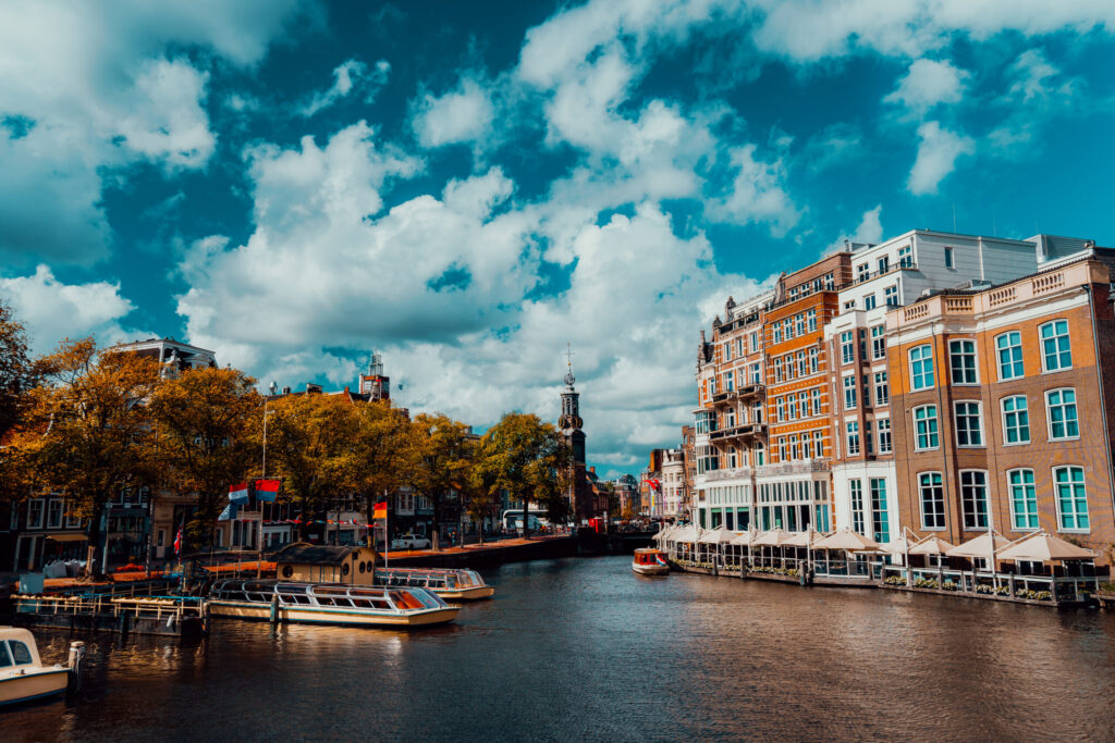 City view of Amsterdam with cruise boats and typical brick houses on sunny day with Vibrant fluffy clouds.