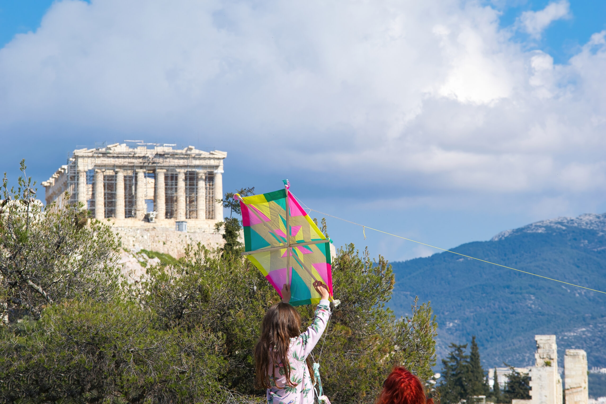 A young girl holding onto a kite as it flies in a deep blue sky . Acropolis , Athens, Greece