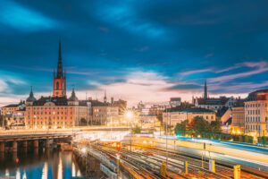 Stockholm, Sweden. Scenic View Of Stockholm Skyline At Summer Sunset. Riddarholm Church And Subway Railway With Train In Blurred Motion.