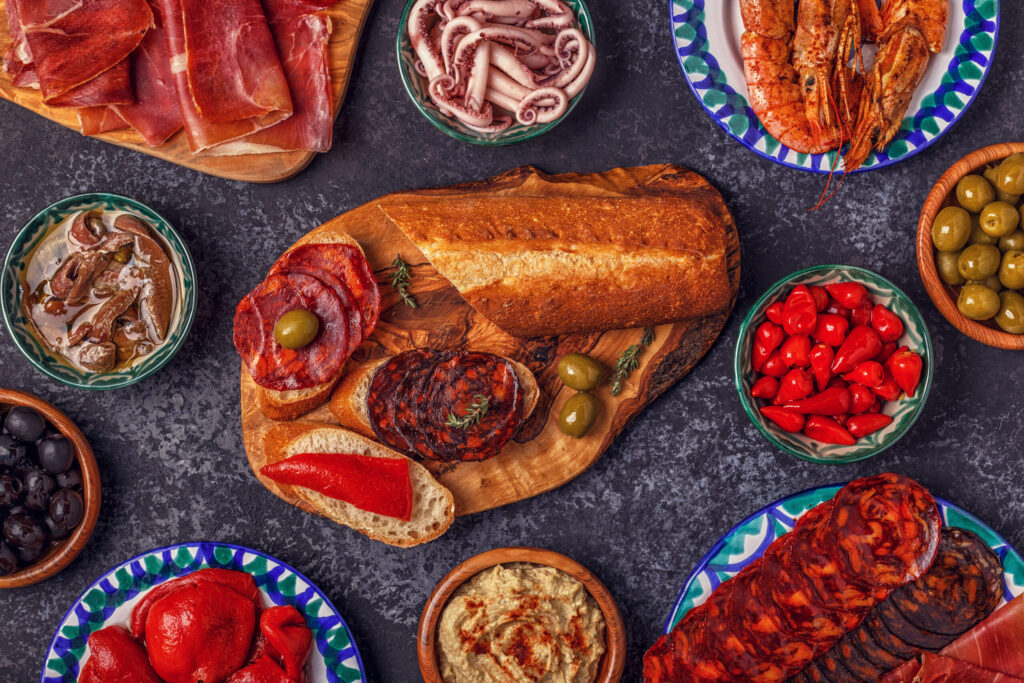 Typical Spanish concept of tapas. The concept includes a variety of pieces of jamon, chorizo, salami, bowls with olives, peppers, shrimps, anchovies, chickpeas puree.