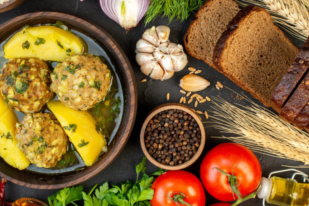 Tasty meatball meal with fresh vegetables, sliced bread, and a bottle of olive oil on a black background