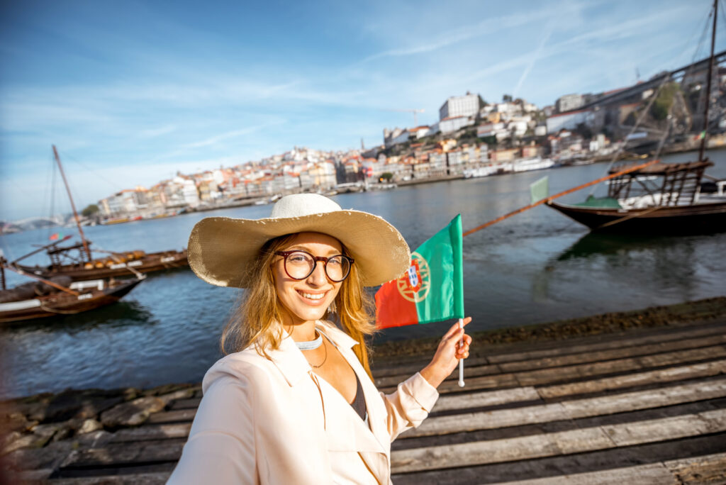 Young woman tourist making selfie portrait with portuguese flag on the beautiful landscape background during the morning light in Porto city, Portugal