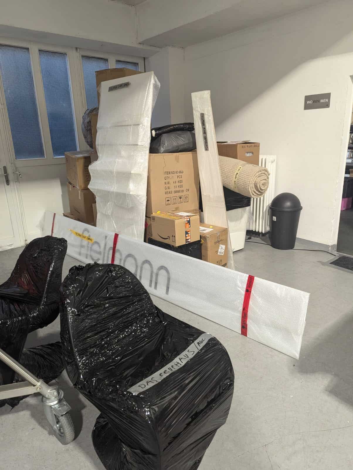 Wrapped furniture pieces and stacked boxes in an indoor hallway, emphasizing cheap removals to Holland.