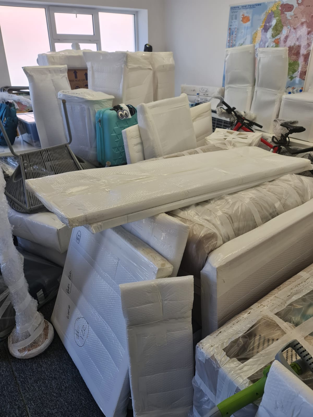 Wrapped furniture and household items packed in a room, protected with foam sheets and plastic wrap ready for transport.