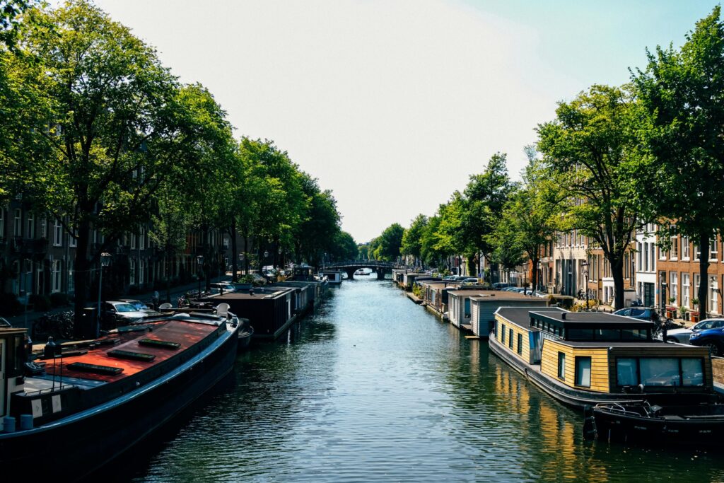 Scenic Amsterdam canal with houseboats and leafy streets on a sunny day – reflecting the question: is Amsterdam expensive to live in