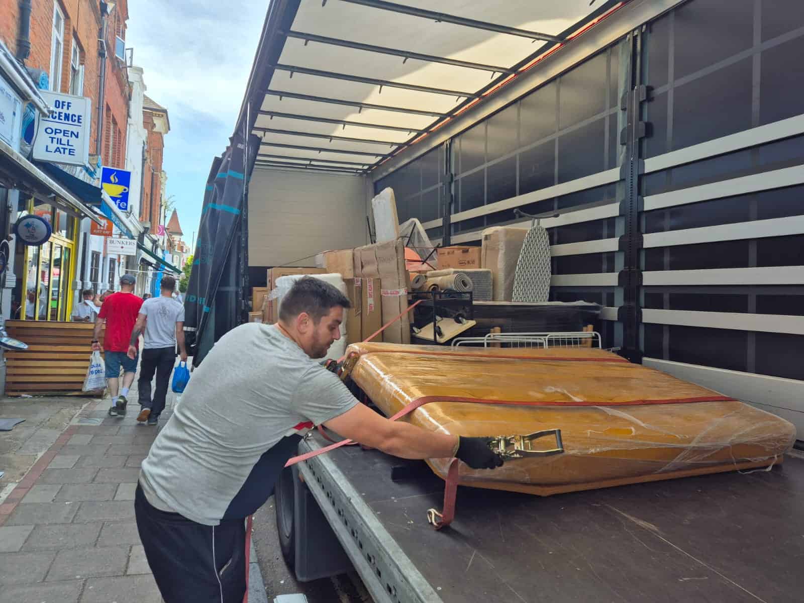 A mover secures a wrapped sofa onto a large transport truck, symbolizing the first step of a family’s journey to their new Dutch home.