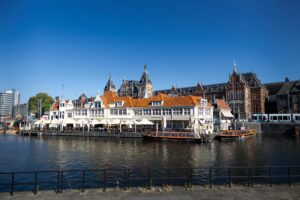 Amsterdam canal scene with orange-roofed waterfront buildings and tour boats – is the netherlands cheaper then germany