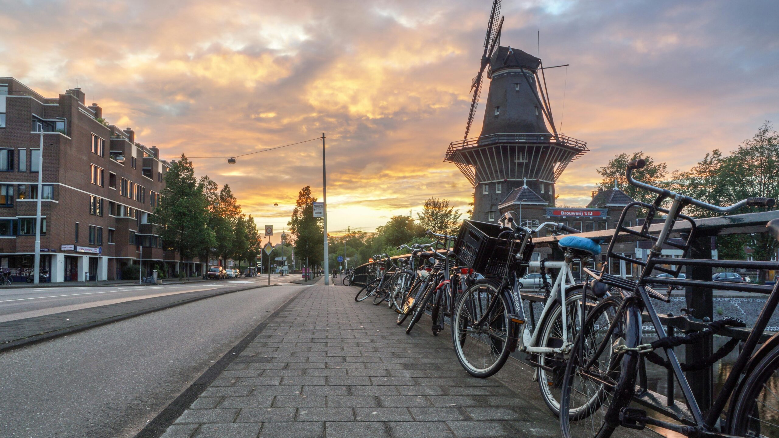 Sunset over a Dutch windmill and riverside bike racks, highlighting the serene, bike-friendly lifestyle that makes the Netherlands ideal to live.