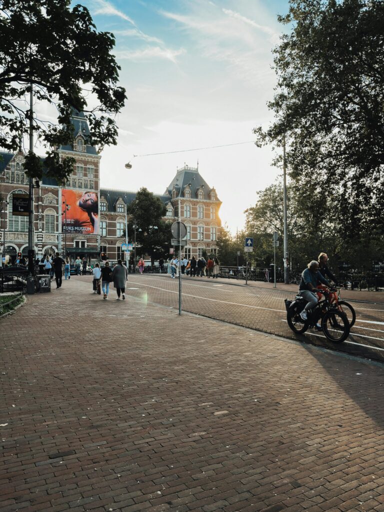 Historic Rijksmuseum façade by a tree-lined street with cyclists at sunset – is the netherlands cheaper then germany