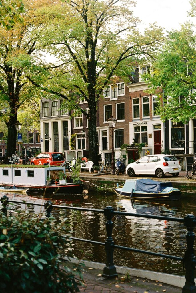 Boats moored on a leafy Amsterdam canal beside historic canal houses and bicycles, illustrating why the Netherlands is a great place to live.