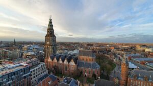 Aerial view of a Dutch city featuring a Gothic church tower and red-roofed buildings, showcasing cityscapes in life in the Netherlands.
