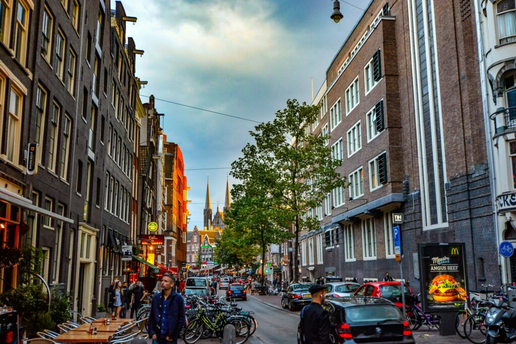 Lively Amsterdam street with people walking, bicycles parked, and historic Dutch buildings, showcasing urban life in the Netherlands.