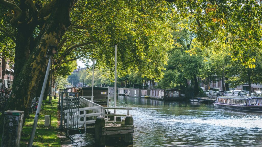 Peaceful canal scene in the Netherlands with trees and houseboats – visualizing the lifestyle contrast in living in France vs Netherlands