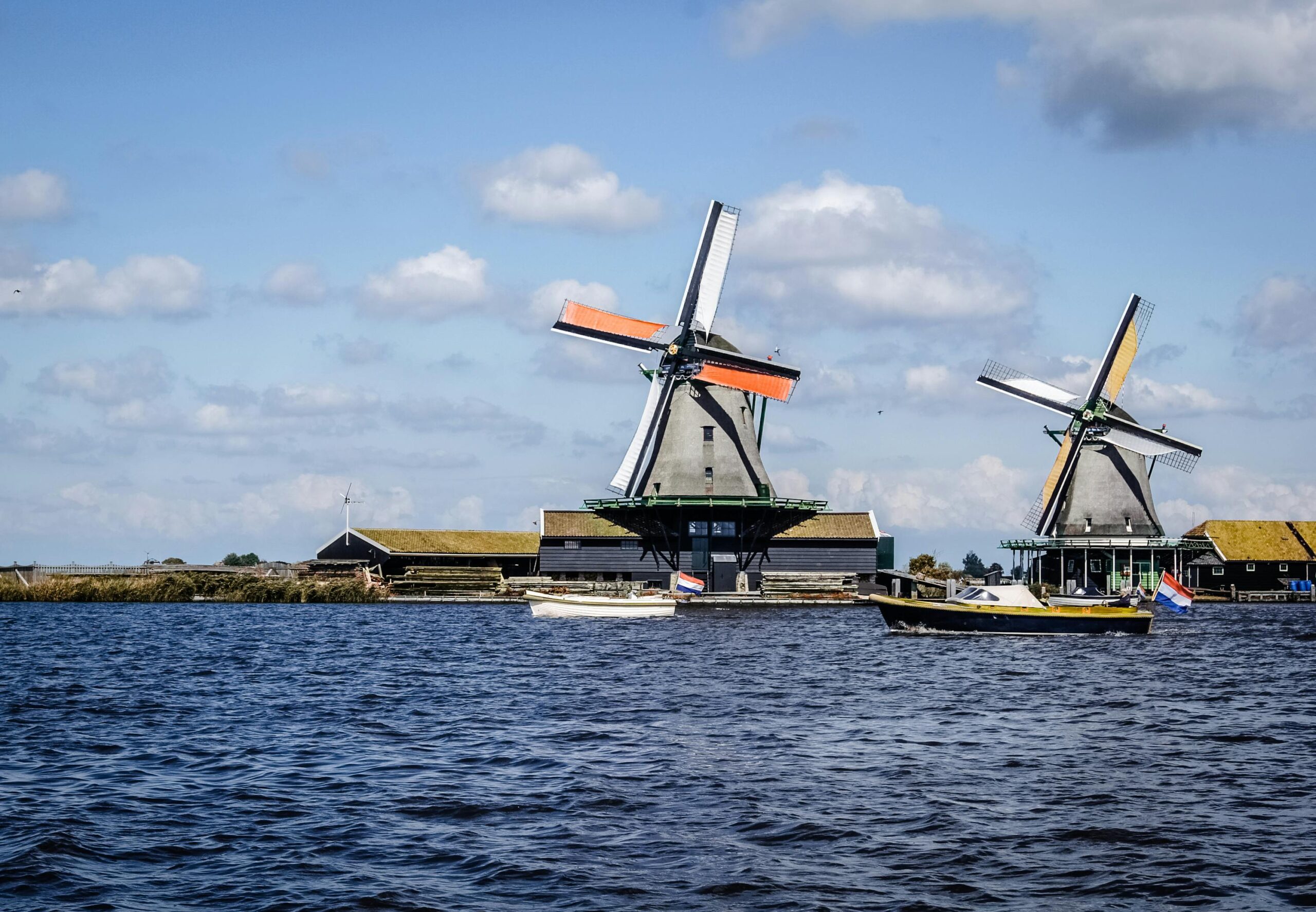 Traditional Dutch windmills on a waterside farm under blue skies—illustrating living in ireland vs netherlands and the iconic Netherlands landscape.