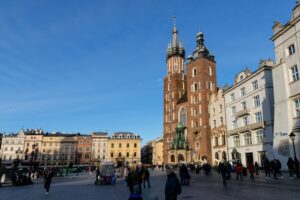 People walking through Kraków’s historic old town square under a clear blue sky, symbolizing the cultural and urban lifestyle of living in Poland vs Netherlands.