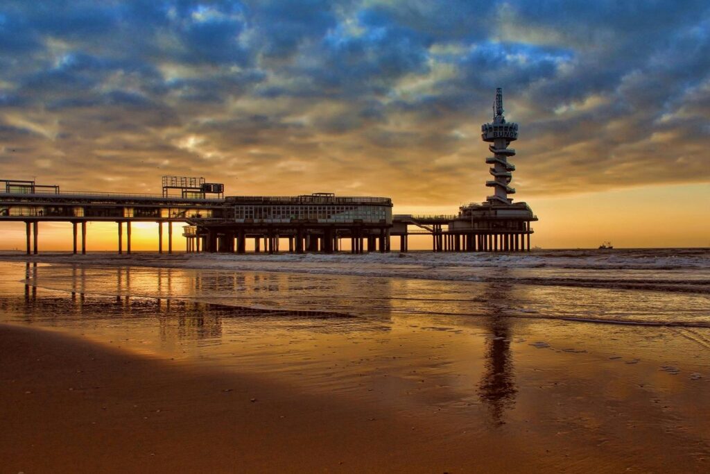 Iconic Dutch coastline with a modern pier during sunset, reflecting the coastal ambiance and urban atmosphere of living in Switzerland vs Netherlands.