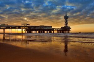 Iconic Dutch coastline with a modern pier during sunset, reflecting the coastal ambiance and urban atmosphere of living in Switzerland vs Netherlands.