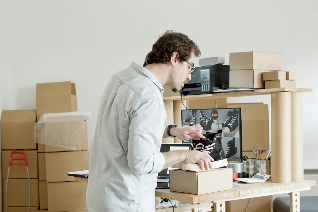 Man carefully packing sneakers into a cardboard box in a home office surrounded by moving boxes – concept of organizing and preparing for a move in the Netherlands.