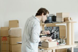 Man carefully packing sneakers into a cardboard box in a home office surrounded by moving boxes – concept of organizing and preparing for a move in the Netherlands.
