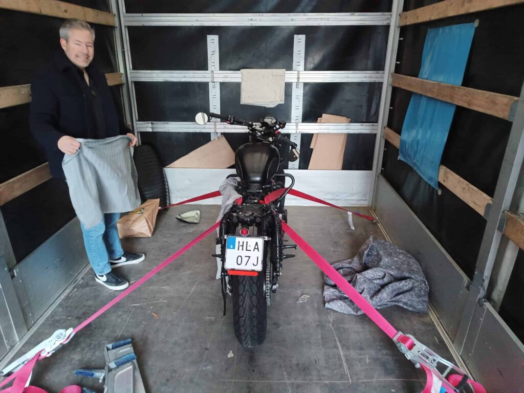 Interior of a moving truck with a motorcycle securely strapped down, prepared for moving from UK to Amsterdam.