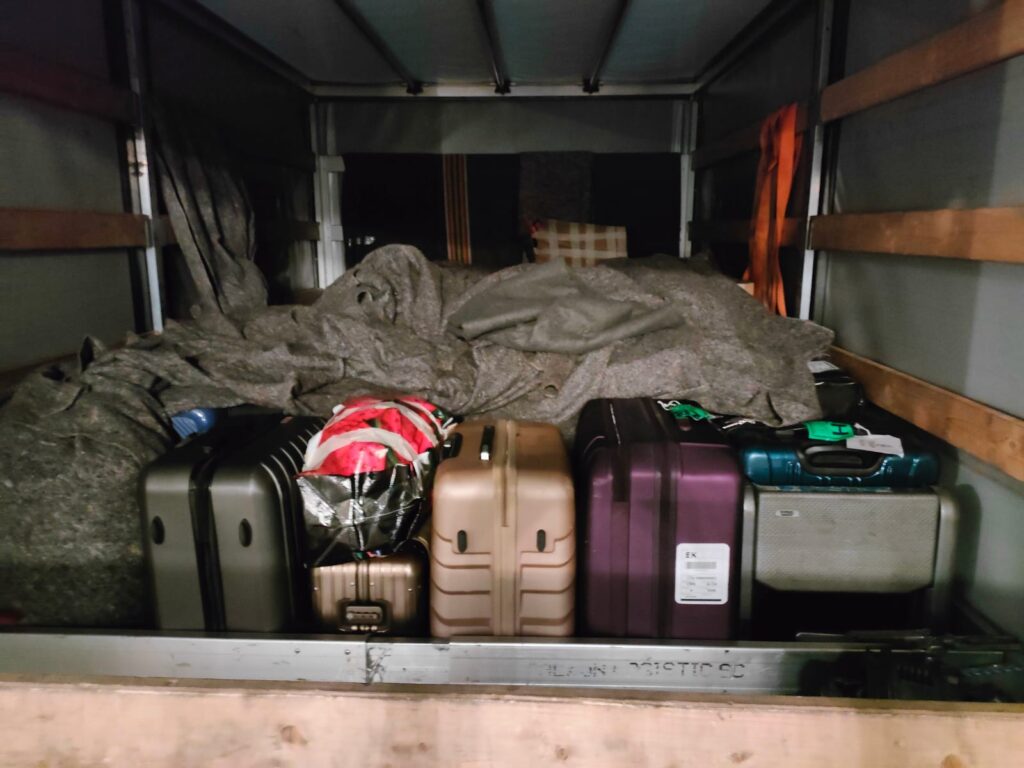 Several suitcases neatly lined up in the back of a moving van wrapped in blankets, illustrating professional packers and movers Netherlands service.