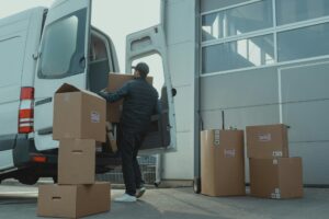 Mover loading fragile boxes into a white van outside a warehouse, showcasing expert packers and movers Netherlands handling.