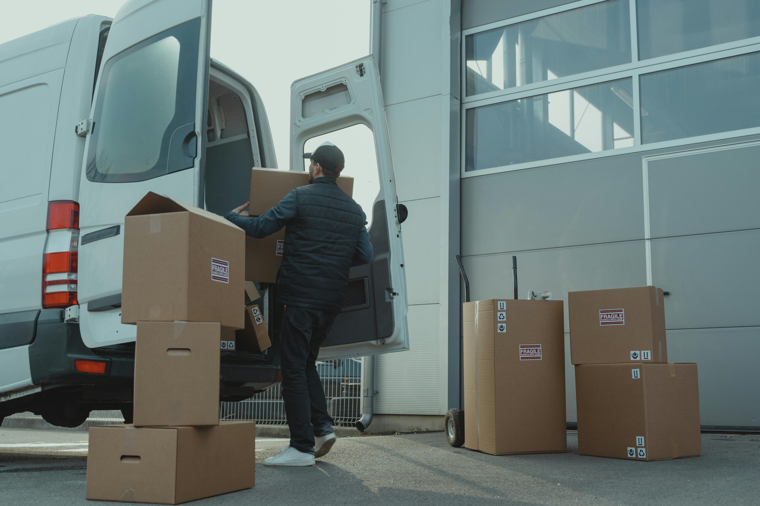 Mover loading fragile boxes into a white van outside a warehouse, showcasing expert packers and movers Netherlands handling.