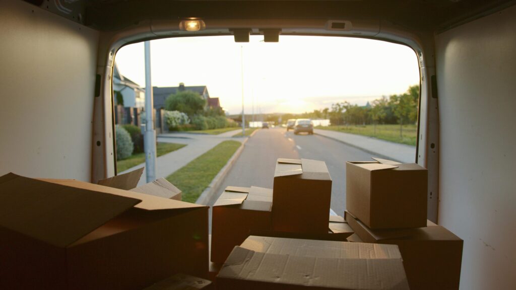 View from inside a van showing multiple packed moving boxes against a backdrop of a quiet suburban street at sunset, representing considerations when moving to the Netherlands.
