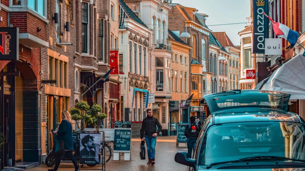 Street scene in a Dutch town with brick storefronts, a moving van unloading equipment, and pedestrians—symbolizing unskilled jobs in the Netherlands for foreigners such as movers, delivery drivers, and retail assistants.