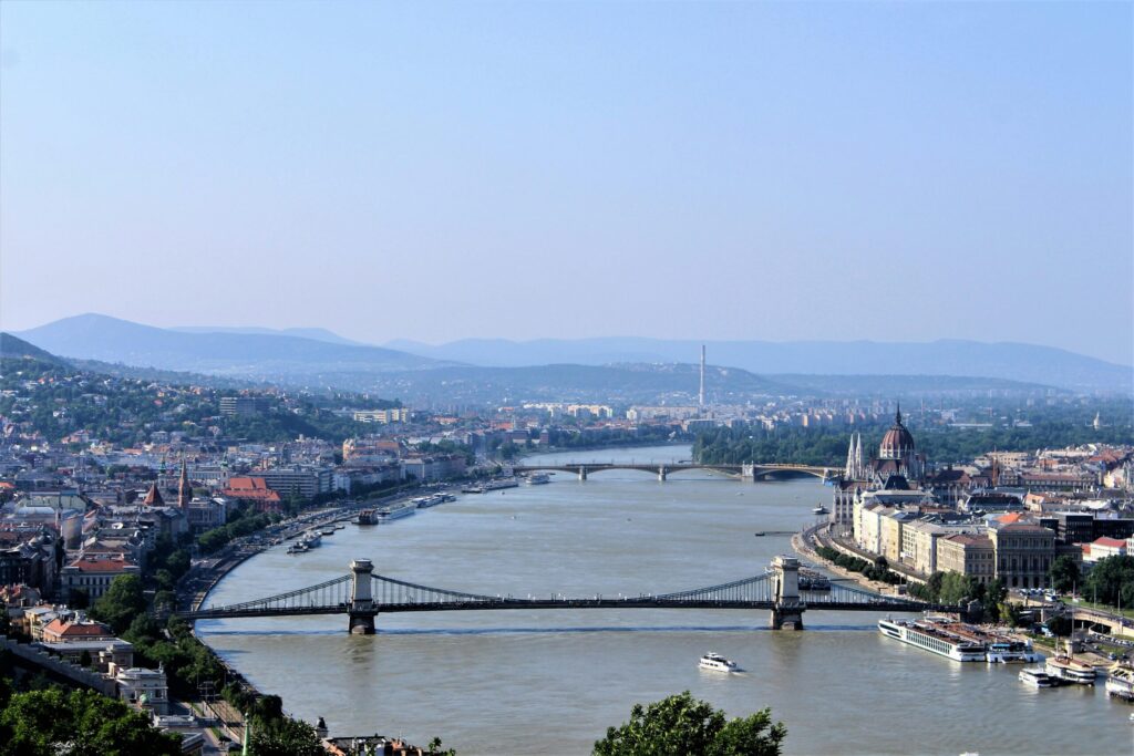 Panoramic view of Budapest with the Danube River, the Chain Bridge, and the Hungarian Parliament Building in the distance.