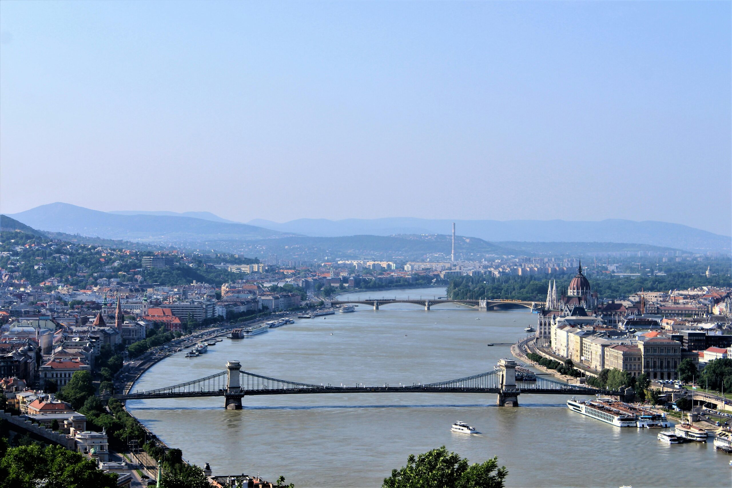 Panoramic view of Budapest with the Danube River, the Chain Bridge, and the Hungarian Parliament Building in the distance.