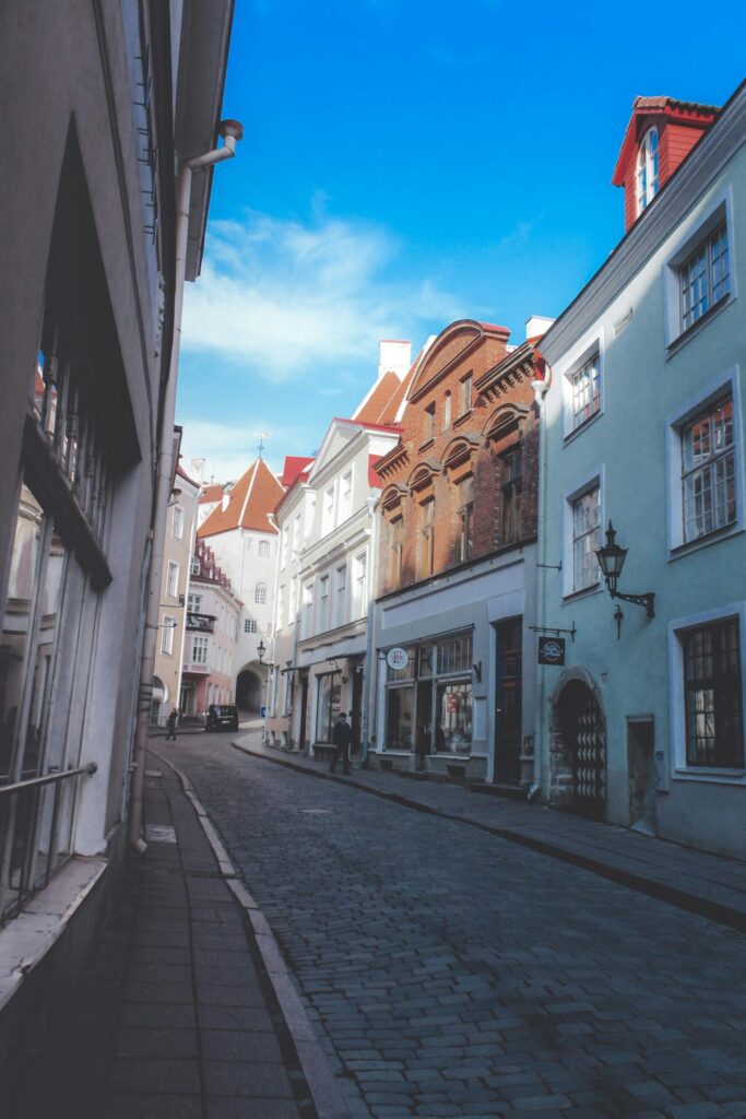 Cobblestone street in Tallinn old town with pastel buildings, shopfronts, and a bright blue sky.