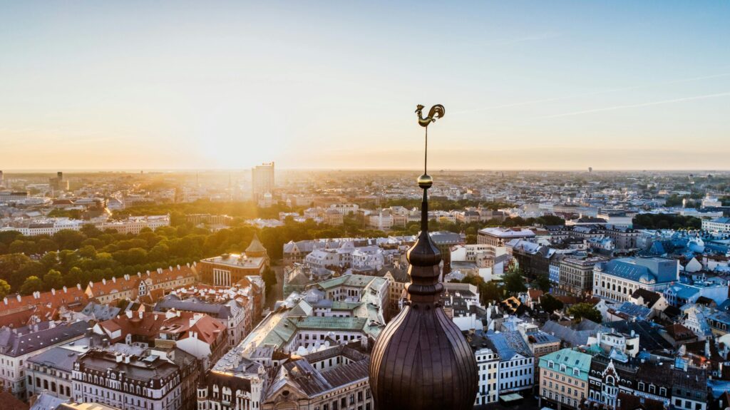 Sunset view over Riga with a tall church spire in the foreground and the old town rooftops stretching toward the horizon.