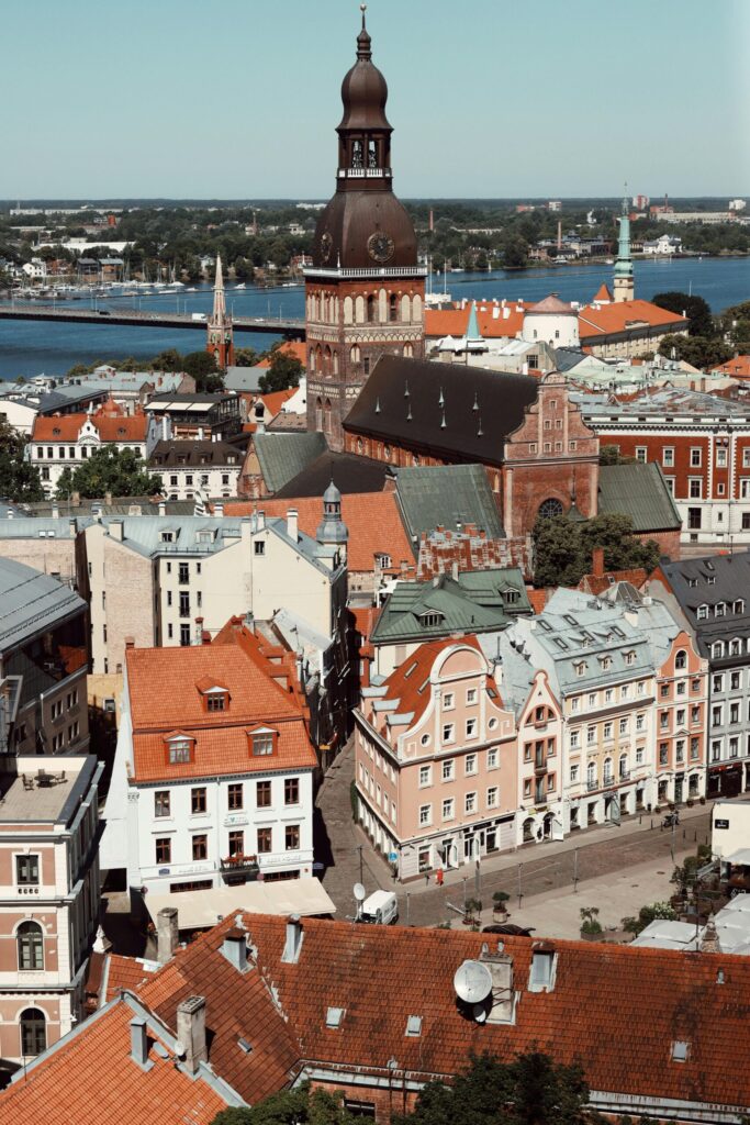 View of Riga old town with red rooftops and a historic church tower in the foreground, with the river and city skyline in the background.