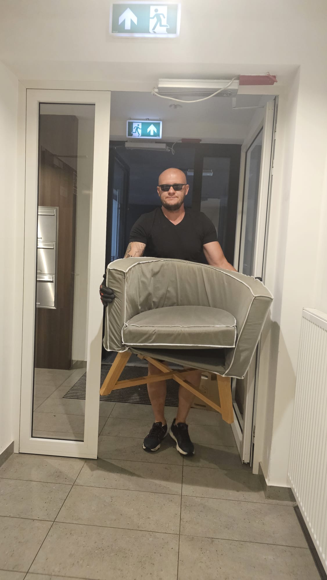 Professional mover carrying a grey armchair through an apartment hallway