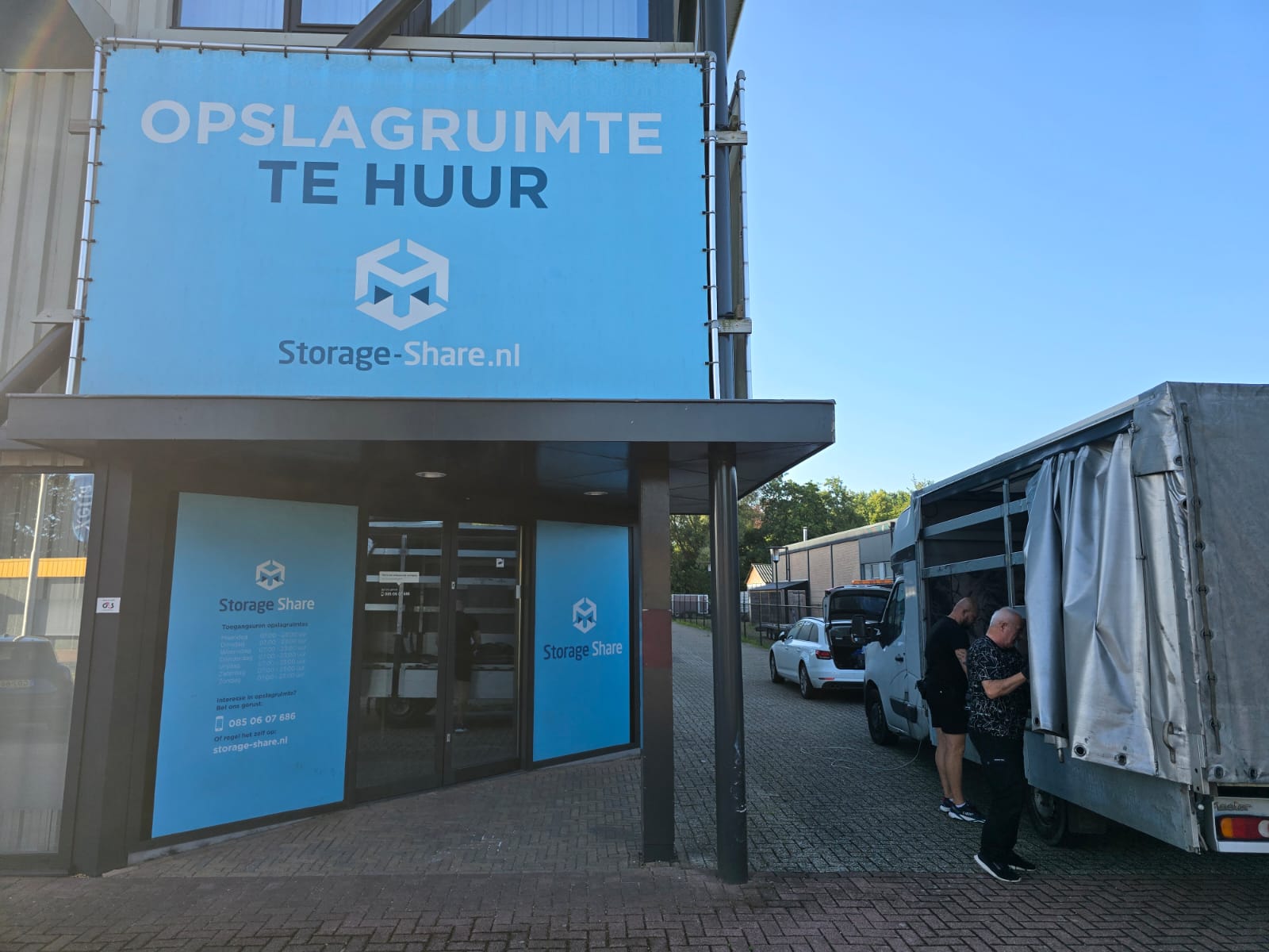 Entrance of the Storage Share warehouse with a large blue sign and a moving truck parked in front
