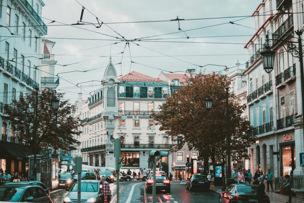 European city street with tram wires, traffic, and historic buildings at dusk in a lively neighbourhood
