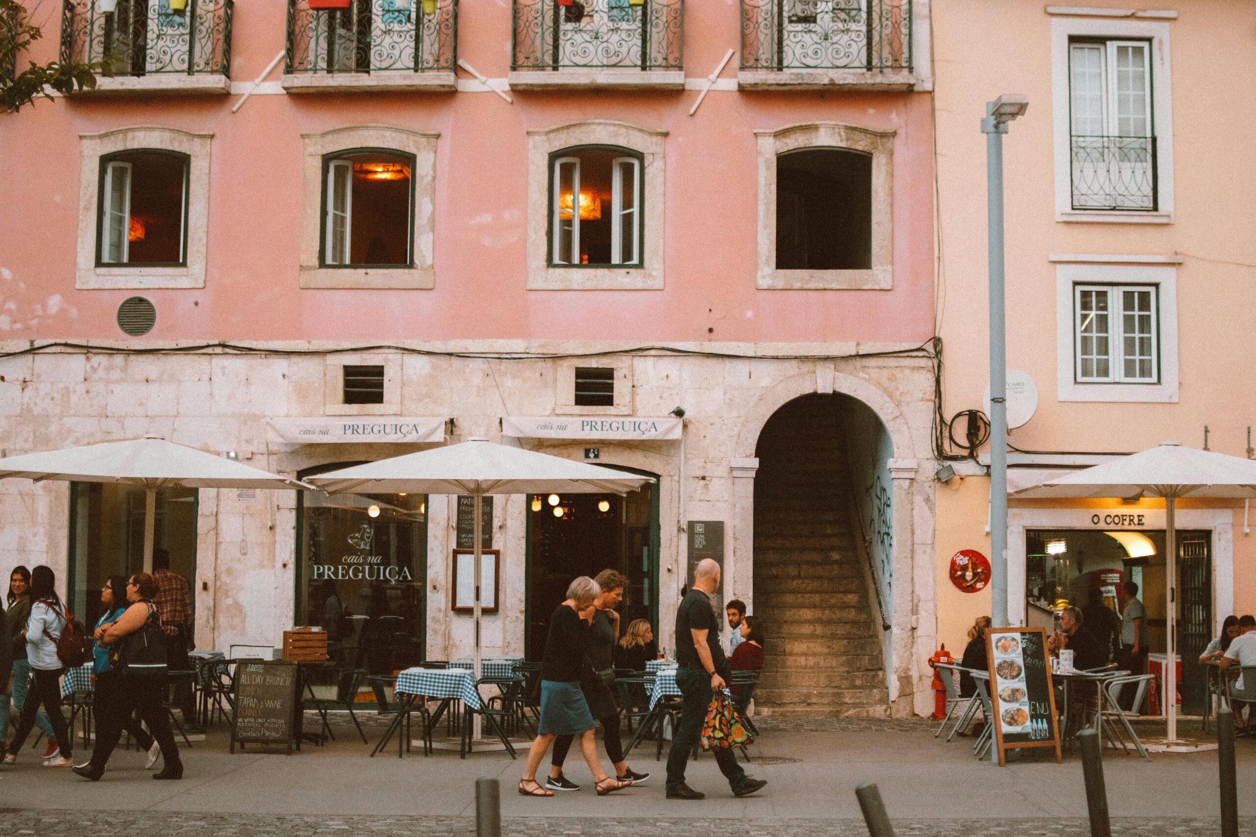 Pink European building facade with street cafes, outdoor tables, and pedestrians in a city square
