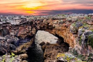 Rocky sea arch on a rugged coastline at sunset, with ocean water flowing beneath the natural bridge