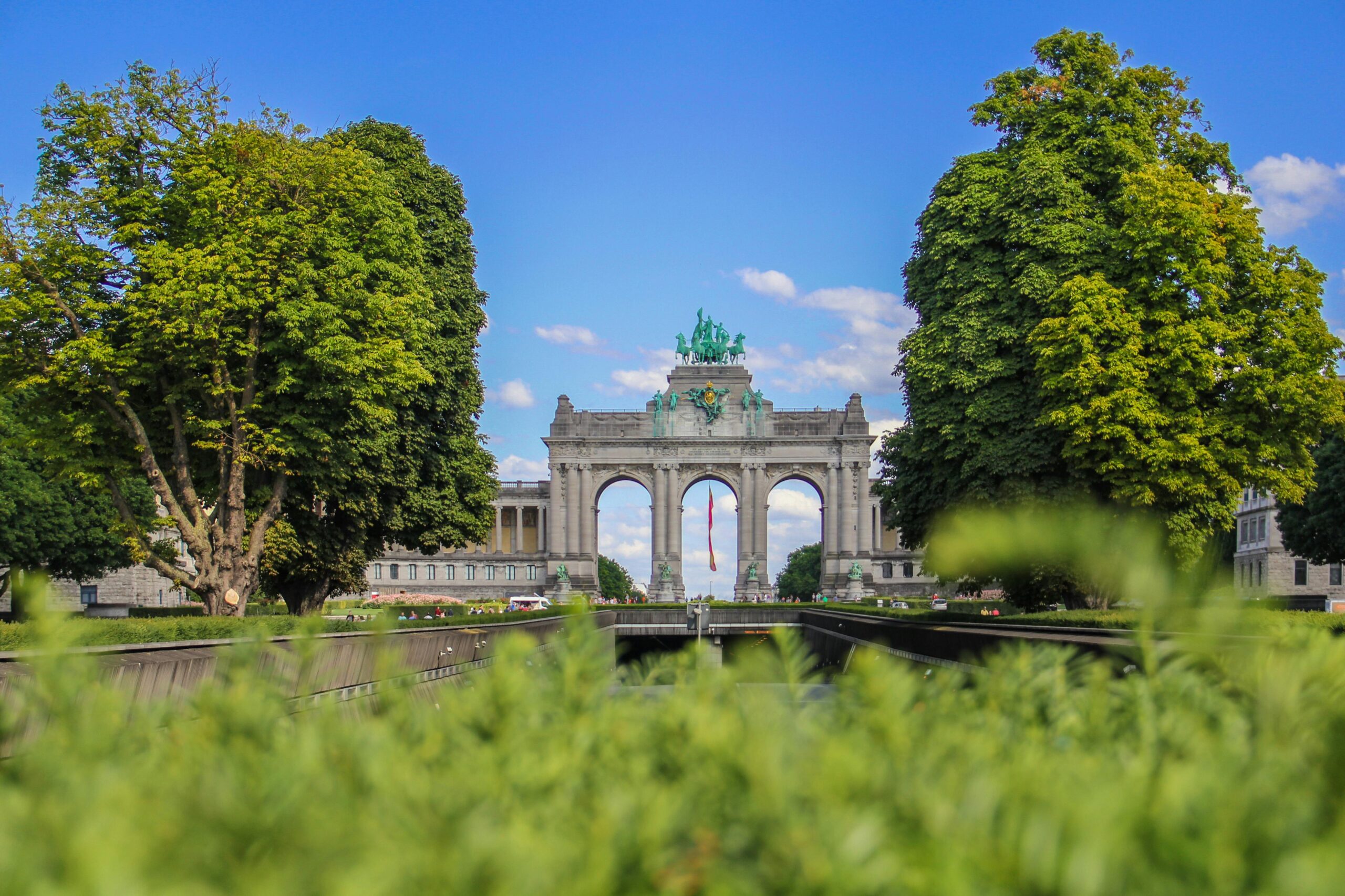 Triumphal arch in Parc du Cinquantenaire Brussels framed by green trees on a sunny day, symbolising moving to Belgium with VANonsite European removals