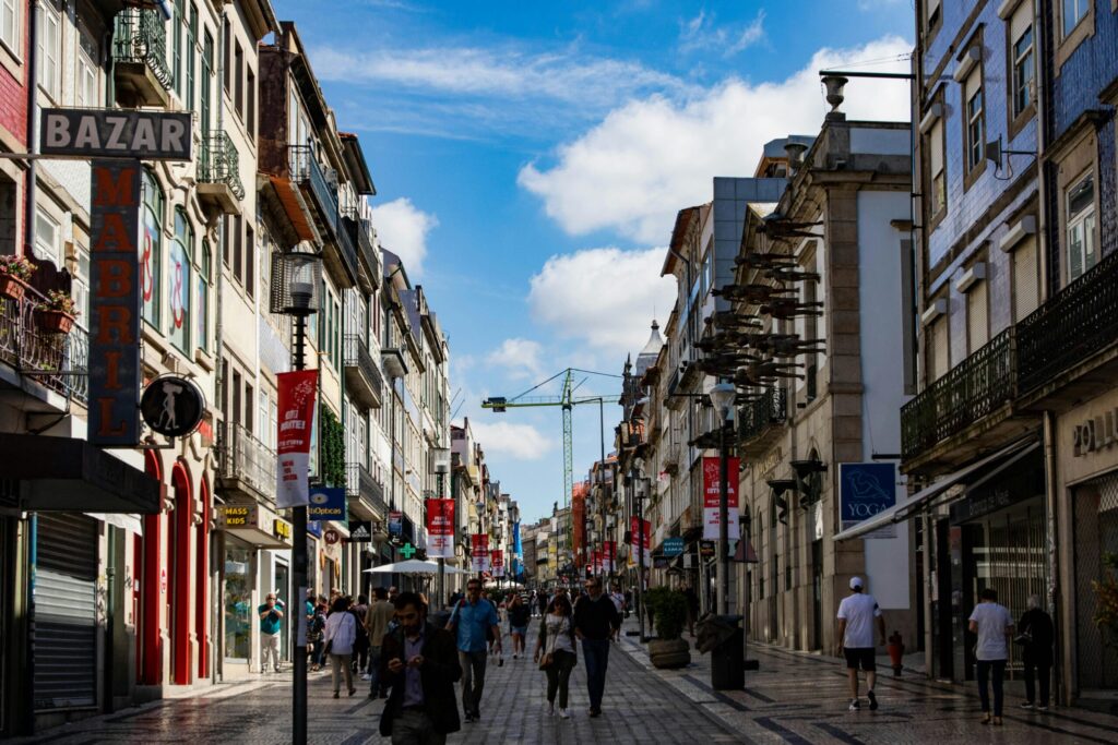 Busy European shopping street with historic buildings, balconies, and pedestrians under a blue sky