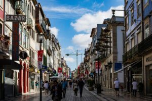 Busy European shopping street with historic buildings, balconies, and pedestrians under a blue sky