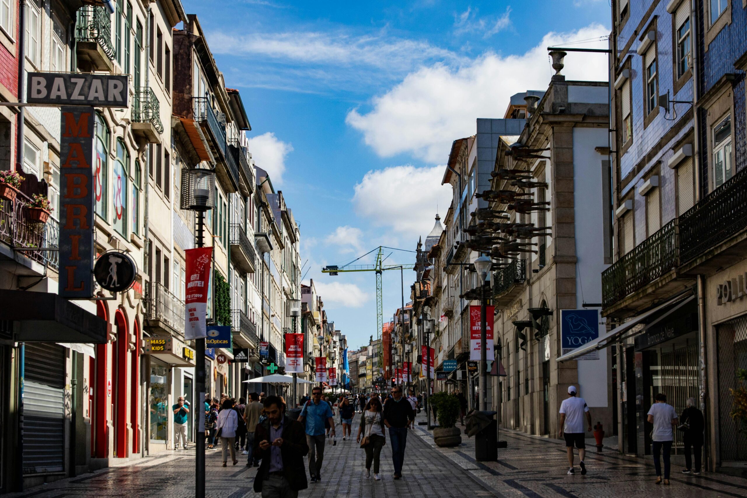 Busy European shopping street with historic buildings, balconies, and pedestrians under a blue sky