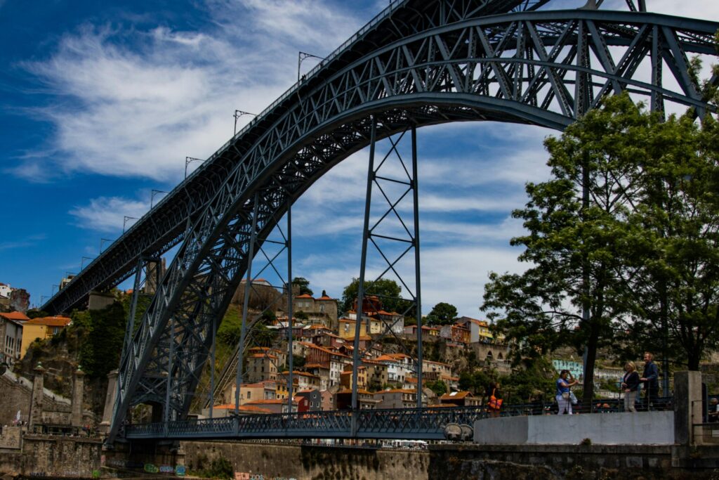Large steel arch bridge over a river with a colourful hillside city and viewpoint under a blue sky